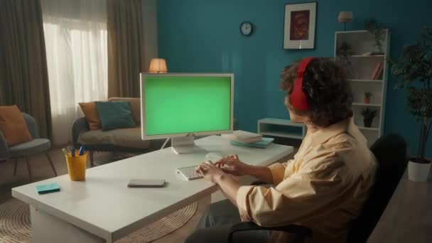 Człowiek Słucha Muzyki Słuchawkami Pracując Przy Komputerze Zielonym Ekranem Facet — Wideo stockowe