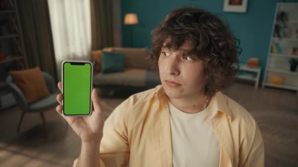 Ung Man Visar Smartphone Med Grön Skärm Nickar Med Huvudet — Stockvideo