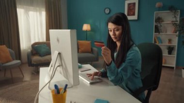 Genç ve çekici bir kız online alışverişleri ödemek için bilgisayar ve kredi kartı kullanıyor. Oturma odasında başarılı bir alışveriş yaptığı için mutlu bir şekilde gülümseyen bir kadının portresi. Gerek yok.