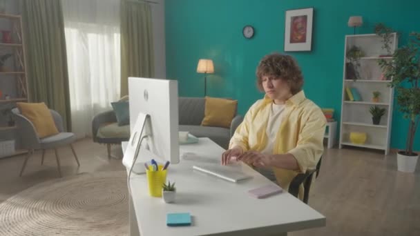 Een Jongeman Spreekt Een Smartphone Terwijl Hij Achter Een Computer — Stockvideo