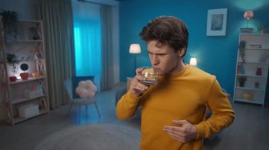 A man with symptoms of a cold is coughing, holding his neck, due to a sore throat close up. A man drinks lemon water to relieve pain. Viral infection, flu, sore throat. Home medicine concept