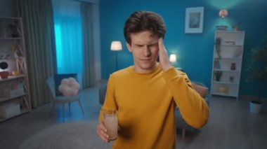 A man throws an effervescent tablet into a glass of water close up. The man puts his hand to his temple, trying to relieve the headache, drinks the medicine. Cure for a cold, pain or hangover. Home
