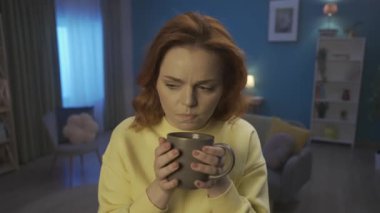A woman adds a slice of lemon to hot tea, blows on the drink, and takes a sip. Woman clutches her cheek, suffering from toothache, tooth sensitivity. Close up. Home medicine concept. HDR BT2020 HLG