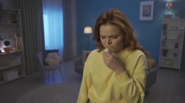 A woman with cold symptoms stands in the living room close up. The woman coughs, blows her nose with a paper handkerchief. A woman uses a nasal spray for a runny nose, nasal congestion, takes a breath