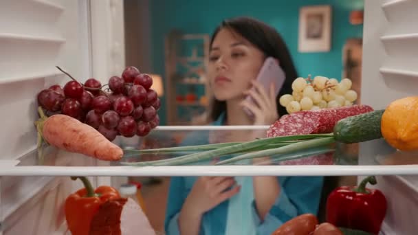 Een Aziatische Vrouw Met Een Telefoon Haar Oor Opent Koelkastdeur — Stockvideo