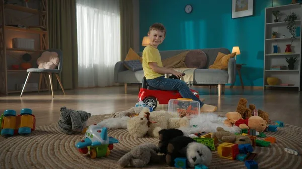Scene of cozy family living room with modern furniture. Many colorful kids toys lscattered around on the floor. The cute little boy driving his red toy car. Smiling and having fun.