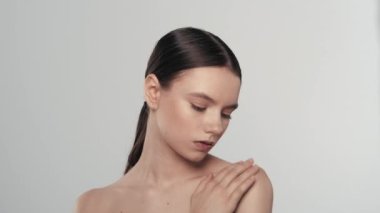 Güzel esmer bir kadın modelin portresi. Kameraya bakan, gülümseyen ve omuzlarındaki pürüzsüz tenine dokunan bir kadını yakından çek. Güzellik derisi reklam konsepti.