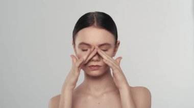 Genç beyaz kadın modelin portresi. Bir kadının kameraya baktığı, pürüzsüz tenine dokunduğu ve göz çevresinden gülümsediği yakın çekim. Güzellik derisi reklam konsepti.