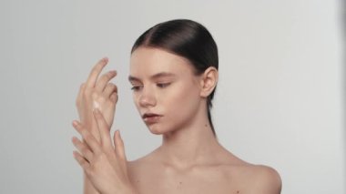 Çekici esmer bir mankenin portresi. Bir kadının kameraya bakıp eline nemlendirici krem sürerken yakın çekim görüntüsü. Beyaz arka planda izole edilmiş. Bakım reklamları konsepti.
