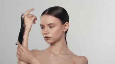 Güzel esmer bir mankenin portresi. Elinde siyah bir tüyle oynayan bir kadının yakın çekim görüntüsü. Beyaz arka planda izole edilmiş. Bakım reklamları konsepti.