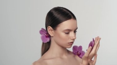 Çekici esmer bir kadın modelin portresi. Kameraya bakıp elinde bir orkide çiçeği tutan bir kadını yakından çek. Saçına çiçek takmış. Organik cilt tanıtım konsepti.