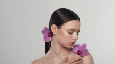 Güzel bir Kafkas esmer modelin portresi. Omzunda orkide çiçeği olan bir kadını yakından çek. Köprücük kemiği bölgesindeki pürüzsüz tenine dokunuyor. Organik cilt reklamı