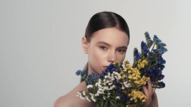 Taze derisi, makyajı ve açık gülüşü olan genç bir kadın modelin portresi. Kurumuş çiçeklerle kameraya bakıp gülümseyen bir kadını yakından çek. Doğal güzellik reklam konsepti.