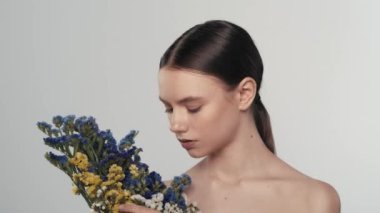 Saf ciltli genç bir kadın modelin portresi. Kurumuş çiçekli bir kadını yakından çek. Parmaklarıyla çiçeklere dokunuyor ve kameraya bakıyor. Doğal güzellik reklam konsepti.