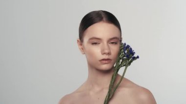 Taze ciltli genç bir kadın modelin portresi. Kurumuş çiçekli bir kadını yakından çek. Çiçeklerle yüzüne dokunmak ve kameraya bakmak. Doğal güzellik reklam konsepti.