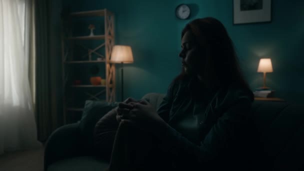在一间昏暗的房间里 一个孤独的年轻女人坐在沙发上 一个女人绝望地思考着个人问题 正在经历一场危机 日日夜夜的变化 时间的转移 — 图库视频影像