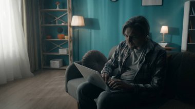 Dizüstü bilgisayar başında çalışan yorgun bir adam, çevrimiçi çalışıyor, oynuyor, pencereden gelen ışıkla aydınlanan karanlık bir odada oturuyor. İnternet bağımlılığı, bir insan çok çalışır. Zihinsel konsept