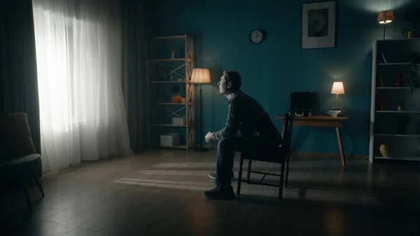 男は部屋の真ん中に椅子に座り 窓の明かりを見ている 暗い部屋に座っている孤独な男の側面 希望のコンセプト メンタルヘルス — ストック写真