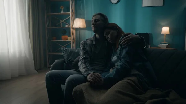 A couple is sitting on a sofa in a dark room close up. A man holds a woman by the hand, hugs. Support for the couple, joint problem solving, reconciliation and understanding in relationships. The