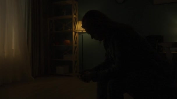 一个女人低着头坐在房间中央靠近黑暗的椅子上 夜复一夜 一个女人抬起头 看着窗外的灯光 时间的短暂 — 图库视频影像