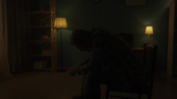 Homem Senta Com Cabeça Curvada Numa Cadeira Meio Sala Escuridão — Vídeo de Stock
