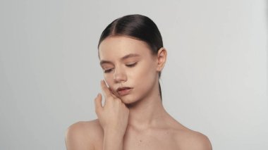 Taze ciltli ve doğal makyajlı güzel bir kadın modelin portresi. Kapalı gözlü bir kızın yanağına dokunuşunu yakından çek yumuşak tenine. Cilt bakımı reklam kavramı.