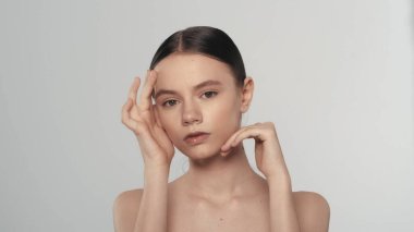 Zarif bir esmer kadın modelin portresi. Kolları havada bir kadının elmacık kemiklerindeki yumuşak tenine dokunup kameraya bakarken yakın çekim görüntüsü. Güzellik derisi reklam konsepti.