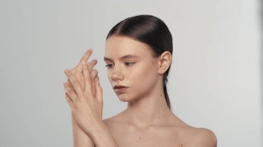 Çekici beyaz bir modelin portresi. Genç bir kadının kameradan kafasını çevirdiği ve eline nemlendirici krem sürdüğü yakın çekim. Bakım reklamları konsepti.