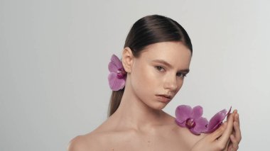 Esmer kadın modelin portresi. At kuyruklu bir kadının orkide çiçeğini elinde tutarken ve kameradan uzağa bakarken yakın plan çekimleri. Organik cilt tanıtım konsepti.