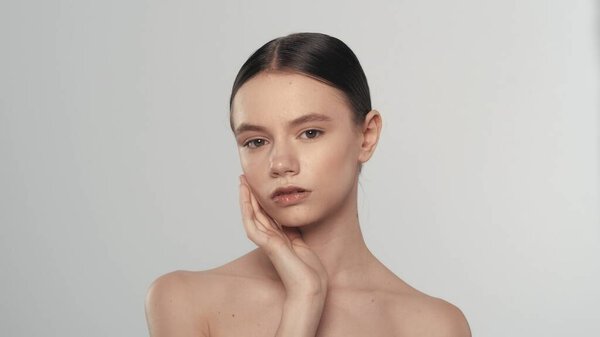 Портрет кавказской модели с натуральным макияжем и хвостиком. Крупный план женщины, касающейся ее лица мягкой кожи и смотрящей в камеру. Концепция рекламы Skincare.