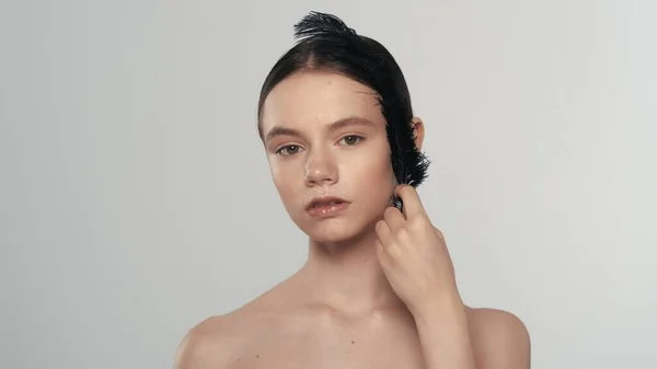 迷人的黑发女人的画像 一个漂亮模特的近照 看着相机用黑色羽毛触摸着她的脸 被白色背景隔离 美容广告概念 — 图库照片
