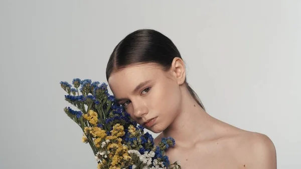 ヌードメイクで若い女性モデルの肖像画 カメラを見ているカラフルな乾いた花の花束を抱えている女性の近くのショットは彼女の頭を回します ビューティー広告コンセプト — ストック写真