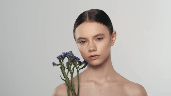 柔らかく肌のある若い女性モデルの肖像画 乾いた花を持つ女性のショットを閉じます 彼女の顔を花で触り カメラを見つめている ニース広告コンセプト — ストック写真