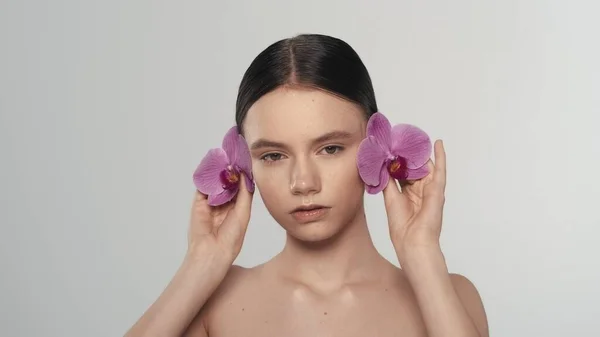迷人的黑发女模特的肖像 一个女人的近照 她的耳朵上挂着兰花 看着摄像机 有机发型广告概念 — 图库照片