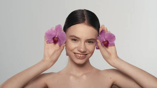迷人的黑发女模特的肖像 一个女人的近照 她的耳朵上挂着兰花 看着镜头笑着 有机发型广告概念 — 图库照片