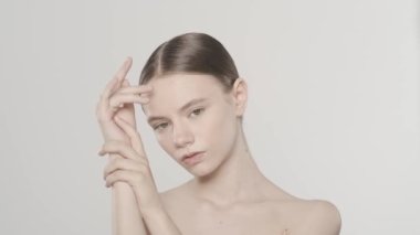 Güzel bir esmer modelin portresi. Beyaz bir kadının kameraya bakıp, ellerinin pürüzsüz tenine dokunuşunu yakından çek. Güzellik el bakımı reklam konsepti. Ağır çekim. HDR