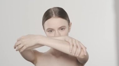 Çekici esmer modelin portresi. Beyaz bir kadının kameraya bakarken, kollarını kavuşturup, ellerindeki ve yüzündeki pürüzsüz deriye dokunuşunu yakından çek. Güzellik el işi reklamı.
