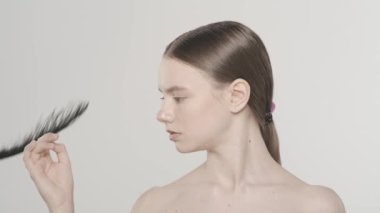 Güzel esmer bir kadın modelin portresi. Tırnaklarına ve eline bakan bir kadının stüdyo fotoğrafını çek. Arkasından siyah tüy düşüyor. El bakımı reklam konsepti. Ağır çekim. HDR
