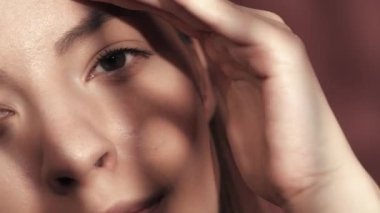 Stüdyoda pembe arka planda çekilmiş bir kadın yüzü. Kadın elini kaşlarının ve göz çevresinin üzerinde gezdiriyor, kırışıklıkların olmadığını gösteriyor. İyi görüş ve göz bakımı