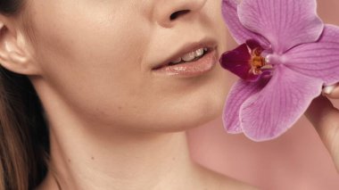 Hassas pembe rujlu kadın dudaklar ve pembe bulanık arka planda orkide çiçeği. Güzel bir gülümseme. Mükemmel kadın yüz makyajı. Ruj izi. Güzellik konsepti, kozmetoloji, cilt bakımı