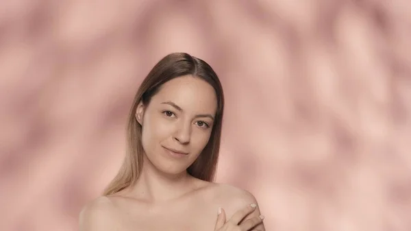若い女性が肩に触れ 滑らかで柔らかい肌を楽しんでいる ピンクのバックグラウンドで孤立した女性の肖像画 化粧品 スキンケア スパのコンセプト — ストック写真