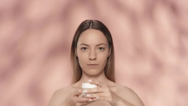 护肤霜 一位年轻的神童女子将一罐面霜或护肤霜放在粉红背景的工作室里 护肤的概念 — 图库照片