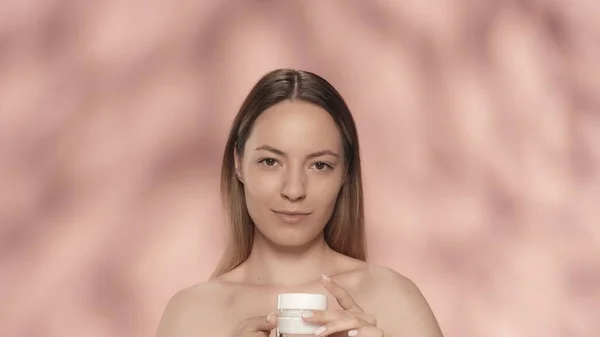 スキンケア用クリーム 若いセミナーの女性は ピンクの背景の近くにスタジオで顔やボディクリームの瓶を保持しています スキンケアのコンセプト — ストック写真