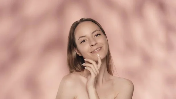 一个有着自然妆容的女人微笑着直视前方 用整洁的手触摸着她的下巴 一个身披粉红背景的精液女子的画像 美丽的概念 自然美 — 图库照片