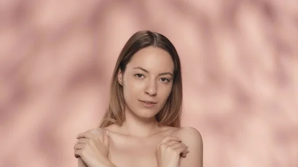 女性は彼女の腕を横切って肩の裸の皮膚に触れる ピンクのバックグラウンドでスタジオで魅力的なセミナーの女性の肖像画 ケアのコンセプト — ストック写真