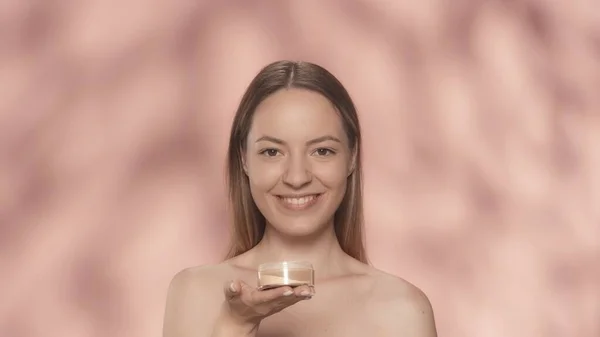 ピンクのバックグラウンドのスタジオで彼女の手に粉の瓶を持った美しいセミナーの女性 化粧をする スキンケアのコンセプト — ストック写真