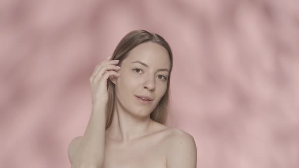 一个女人用手捂住额头 把头发塞到耳朵后面 画室里一个粉红背景的女人的画像 用天然化妆品护肤 — 图库视频影像