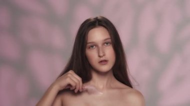 Kafkasyalı genç bir kızın portresi. Köprücük kemiği bölgesinde ve yüzünde tüyle oynayan bir mankenin yakın çekim görüntüsü. Tüyleri yolmak. Cilt bakımı reklam kavramı.