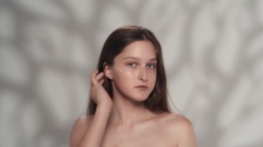 Beyaz kadın modelin çekici portresi. Yüzünde krem olan bir kızı yakından çek. Parmaklarıyla krem sürüyor ve kameraya bakıyor. Güzellik derisi reklam konsepti.