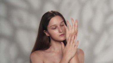 Beyaz tenli esmer modelin portresi. Bir kızın kameraya bakıp eline nemlendirici krem sürdüğü yakın plan bir fotoğraf. Bakım reklamları konsepti.